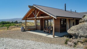 Una cabaña de madera moderna con techo inclinado, ventanas grandes y un patio con mobiliario.