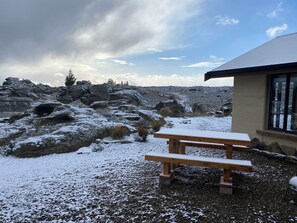 A rocky outdoor area with a wooden picnic table and a building with a window.
