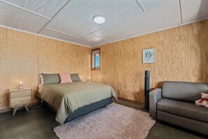 A bedroom with a bed, a nightstand, a lamp, a window, and a sofa.