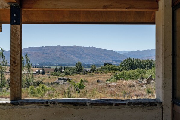 Vista desde una ventana con alféizar de piedra, sobre un paisaje rural con montañas a lo lejos.