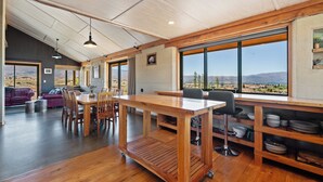 Un comedor amplio con una mesa y sillas de madera, ventanas grandes con vistas al paisaje desértico y una cocina moderna con armarios de madera y una zona de bar.