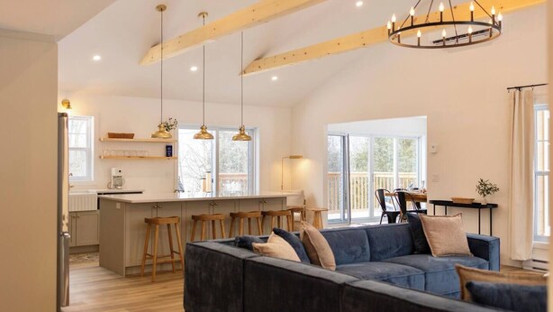 Un salón espacioso con un sofá azul oscuro, vigas de madera y un ventanal grande.