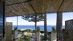 A covered outdoor dining area with a table set for two, overlooking a beach. - Elegant Villa by Fontane Bianche - Beahost Rentals (Syracuse)
