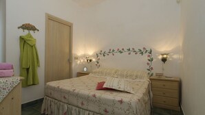 A bedroom with a floral bedspread, a wooden door, a nightstand with a lamp, and a wall-mounted light fixture. - Elegant Villa by Fontane Bianche - Beahost Rentals (Syracuse)