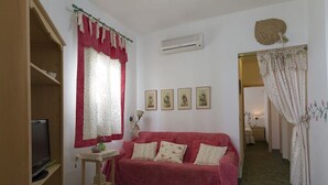 A cozy living room with a red sofa, a television on a wooden stand, and a window with red curtains. - Elegant Villa by Fontane Bianche - Beahost Rentals (Syracuse)