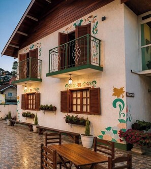 A building with wooden balconies, outdoor seating, and decorative wall art. - Pousada D Paula (Campos do Jordão)