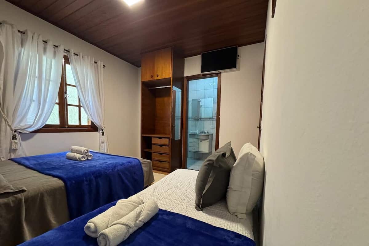A room with two beds, a wooden wardrobe, a small TV, and a window with curtains.