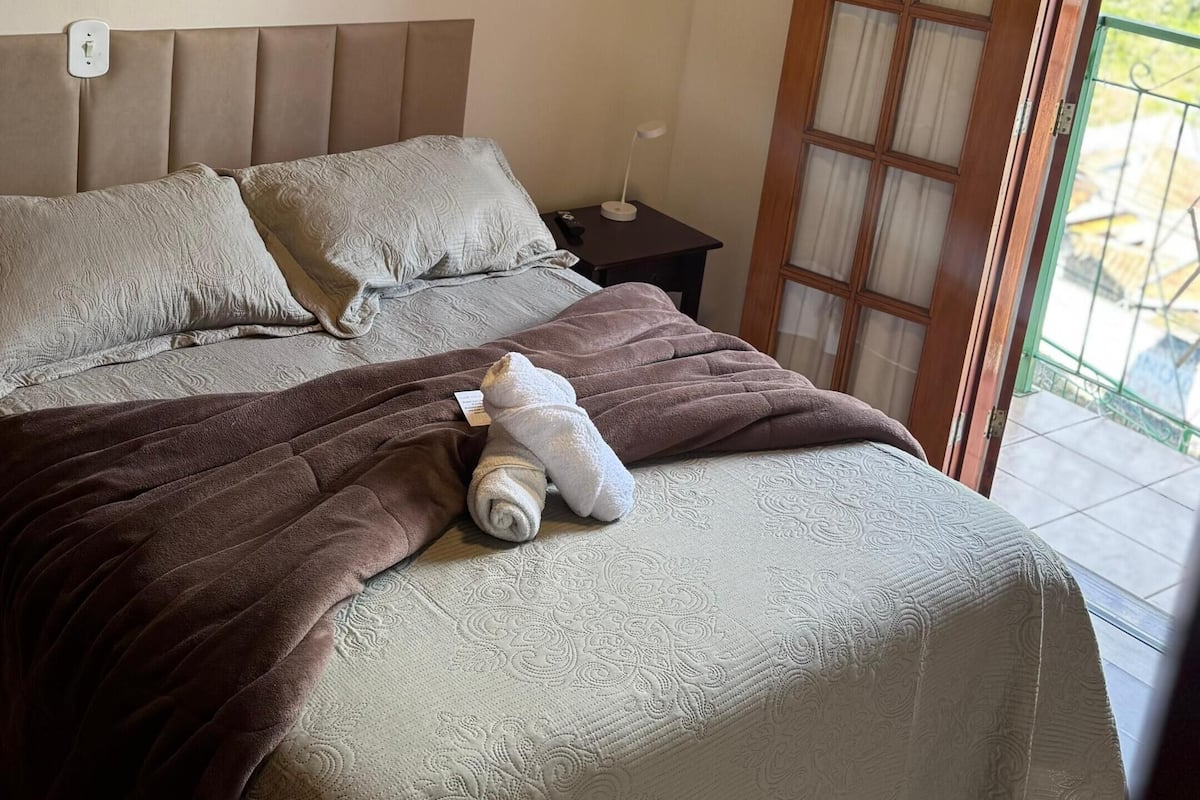 A bedroom with a bed, pillows, a bedside lamp, and a window with a view.