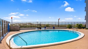 Piscina com grade de metal, cerca de madeira e céu azul límpido.