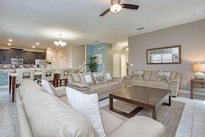 A spacious living room with a large beige sectional sofa, a wooden coffee table, and a dining area with a kitchen in the background. - Beautiful Home With Private Pool in Champions Gate (Davenport)