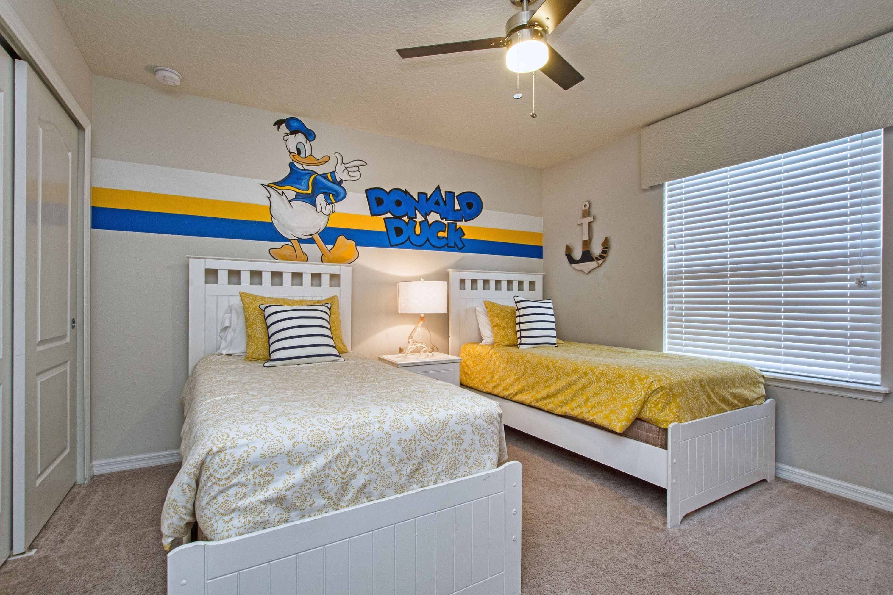 Een slaapkamer met twee bedden, een plafondventilator en een muurschildering van Donald Duck.
