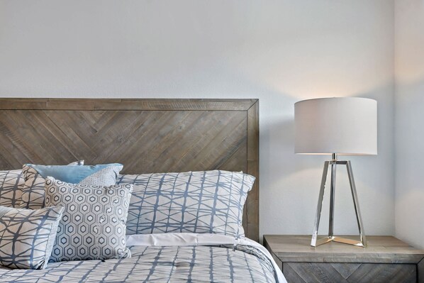 A neatly made bed with patterned pillows and a modern floor lamp beside it.