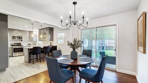 A modern kitchen with stainless steel appliances, a dining area with a round table and blue chairs, and a large sliding glass door leading to a backyard. - Modern, Fully Furnished Retreat, Close to OSU Campus, Downtown and Riverside Hos (Columbus)