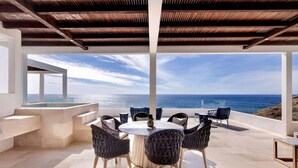 A modern outdoor dining area with a view of the ocean, featuring a round table and wicker chairs. - Oceanfront Penthouse for 8 • 360° Views & Jacuzzi (Los Cerritos)