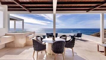 A modern outdoor dining area with a view of the ocean, featuring a round table and wicker chairs.