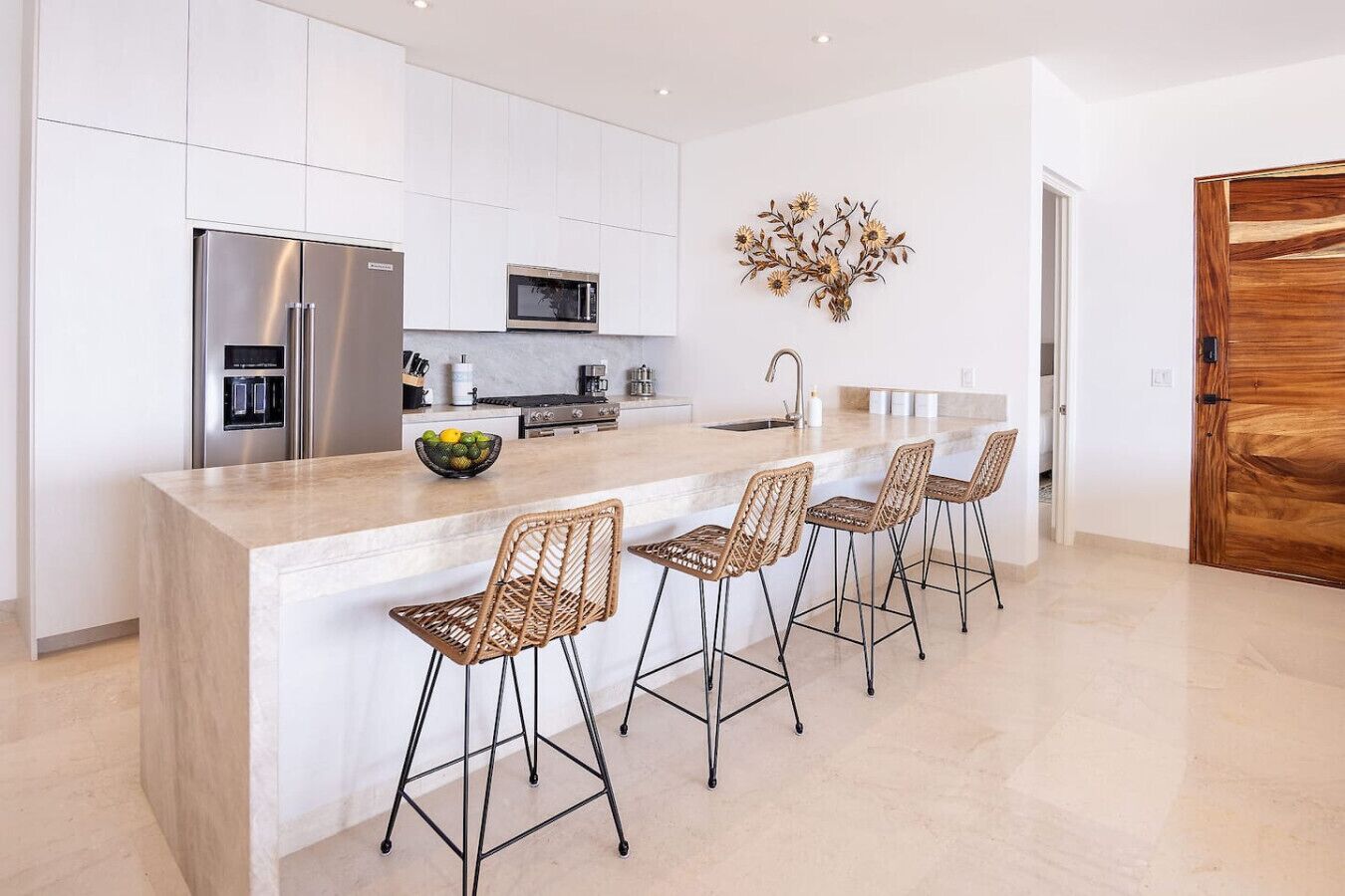 A modern kitchen with white cabinetry, stainless steel appliances, a central island with bar stools, and a decorative wall piece.