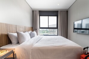 Een hotelkamer met een bed, nachtkastje, televisie en raam met uitzicht over de stad.