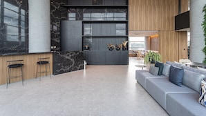 A modern lobby with a grey sofa, black chairs, a reception desk, and a wooden wall. - AV.NU by Viva - Residencial Alto Padrão próximo a Business Center na Nações Unidas. (São Paulo)