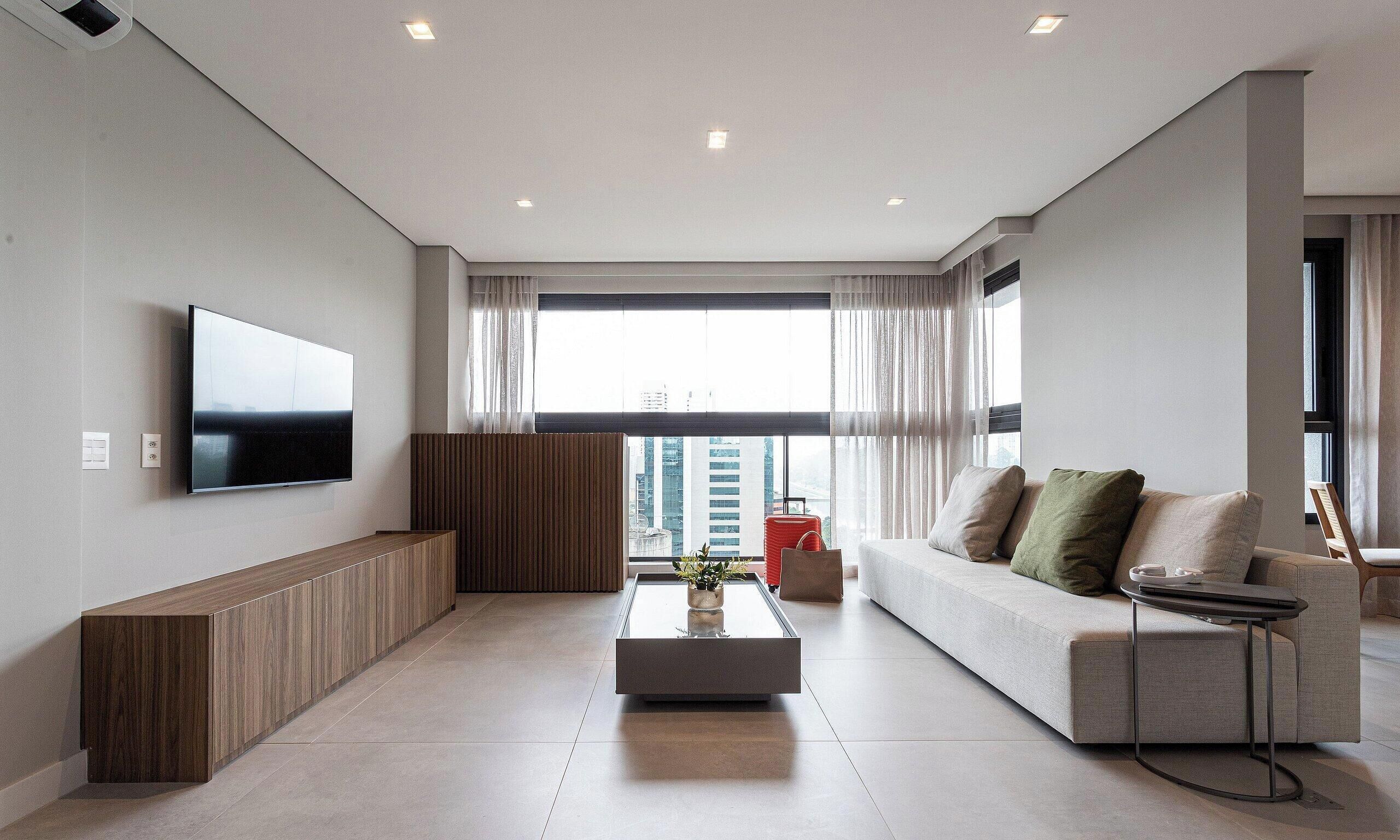 A modern living room with a flat-screen TV, a sofa, a coffee table, and a view of the city.