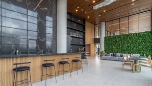 A modern bar area with a wooden counter, black bar stools, and a green wall. - AV.NU by Viva - Residencial Alto Padrão próximo a Business Center na Nações Unidas. (São Paulo)