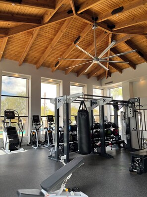 A gym with various exercise equipment, large windows, and a wooden ceiling.