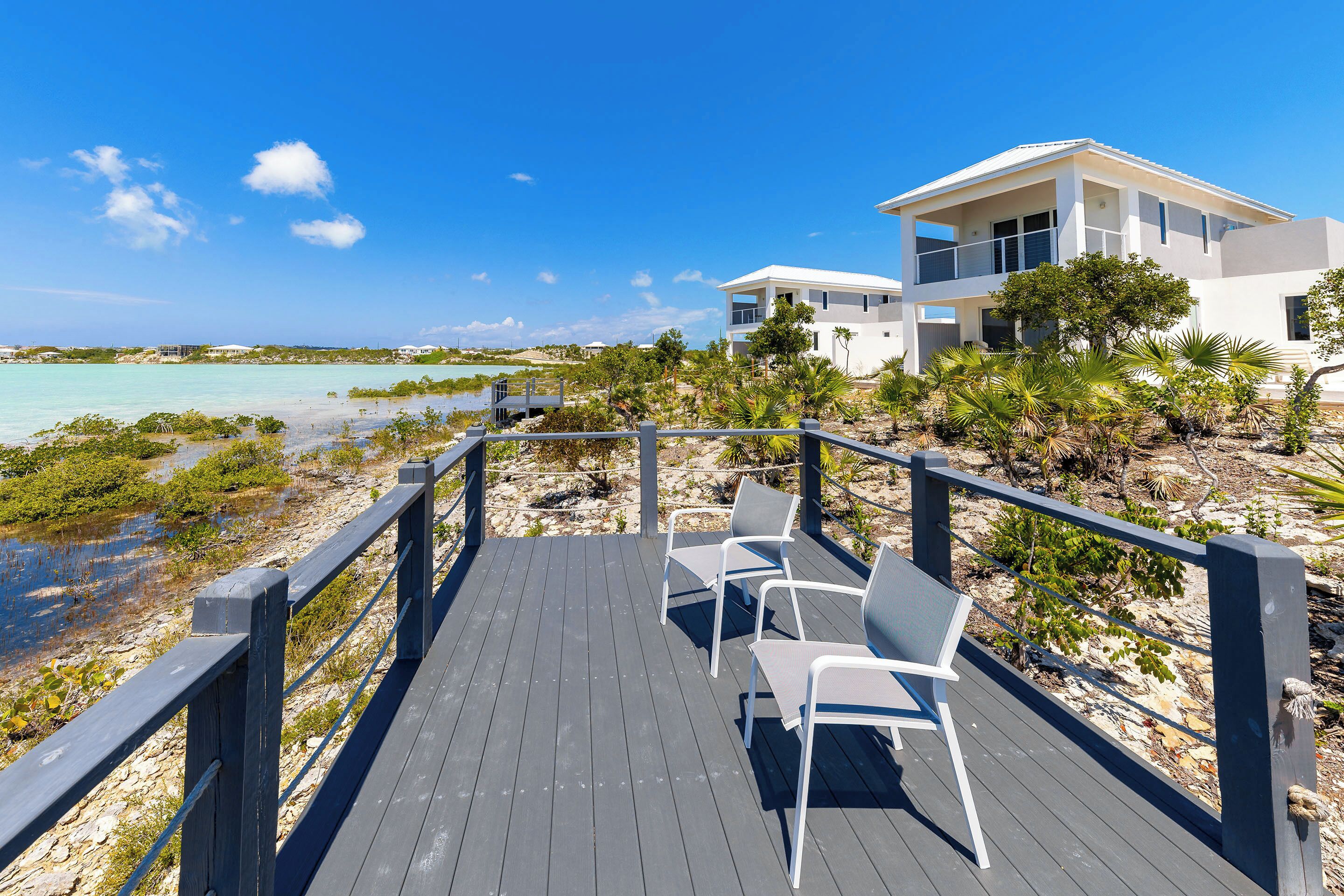 A modern beach house with a wooden deck and chairs overlooking the ocean.