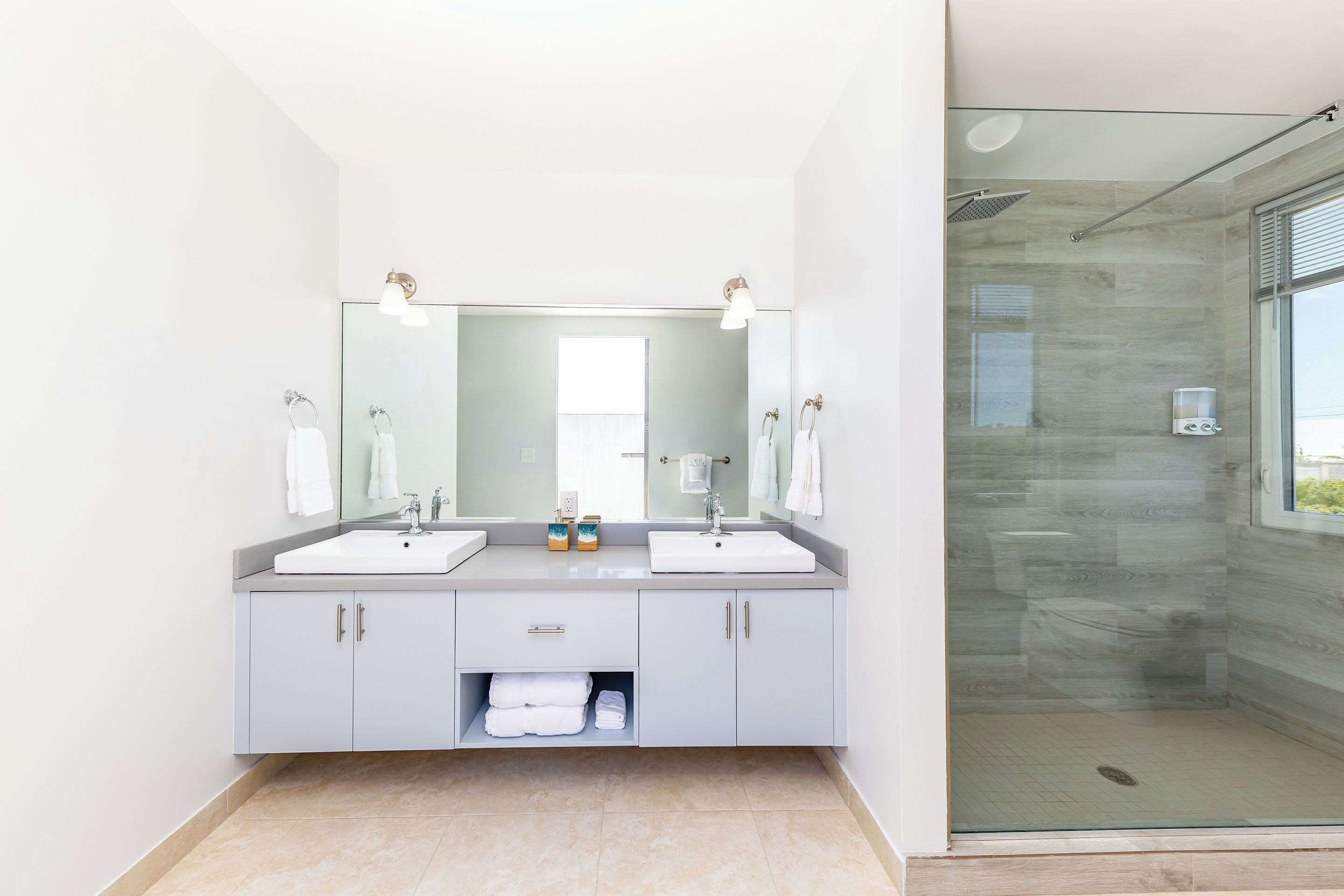 A modern bathroom with two sinks, a large mirror, and a glass-enclosed shower.