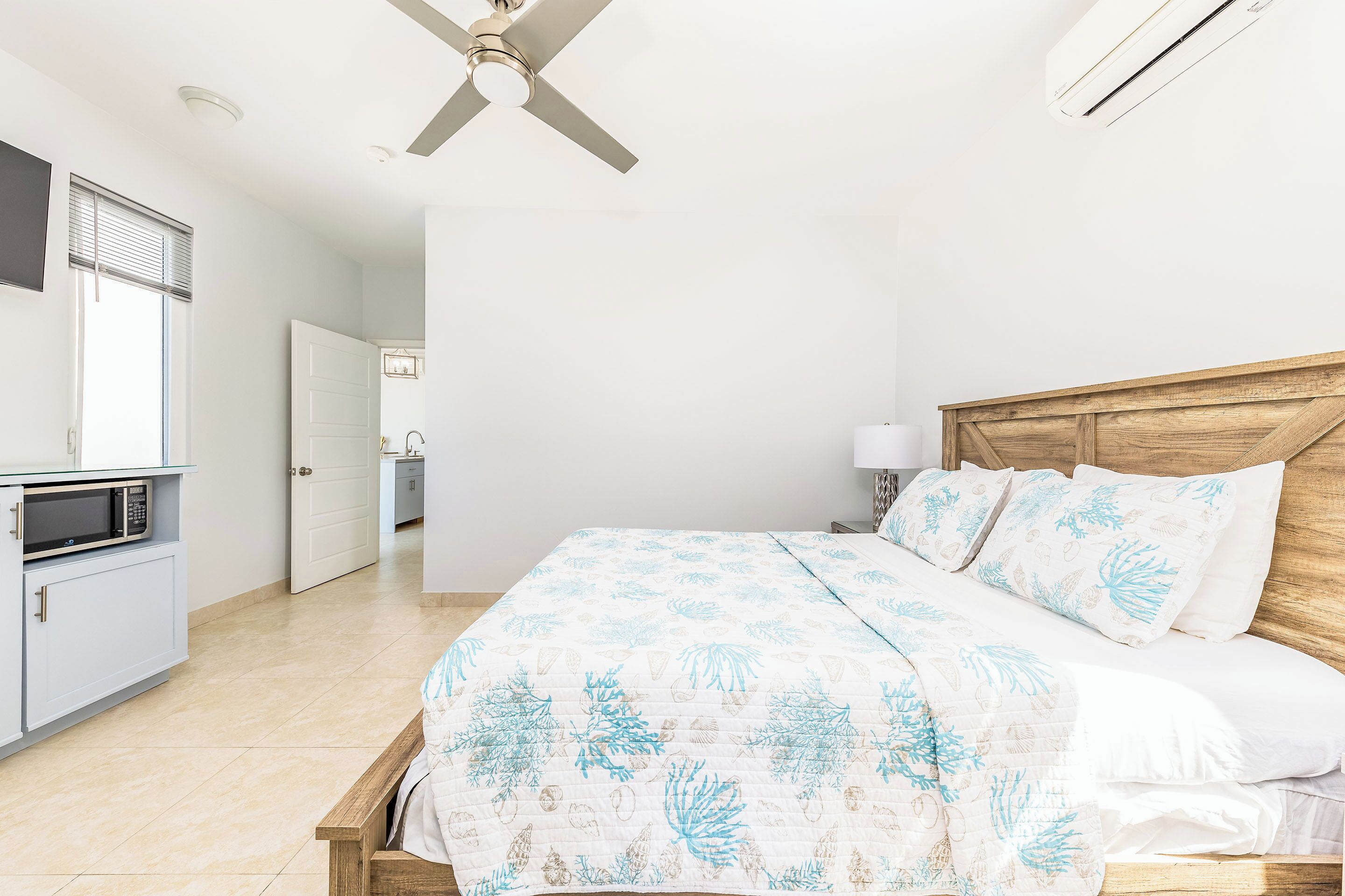 Ein Schlafzimmer mit einem Bett, einem Deckenventilator, einer Mikrowelle und einer Tür zu einem anderen Raum.