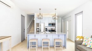 Una cocina moderna con una isla central, taburetes de bar e iluminación colgante.