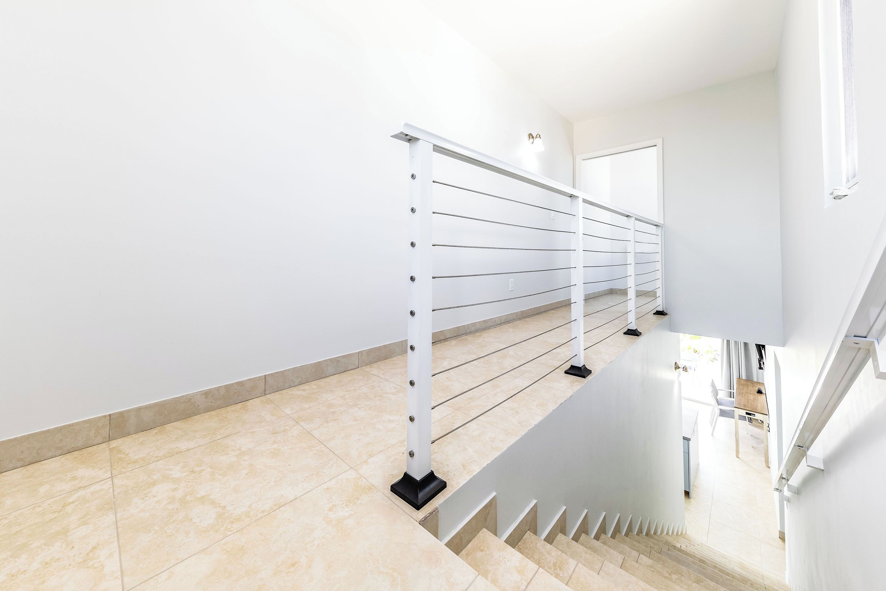 A modern staircase with a metal railing, beige tiled flooring, and a view of a dining area in the background.