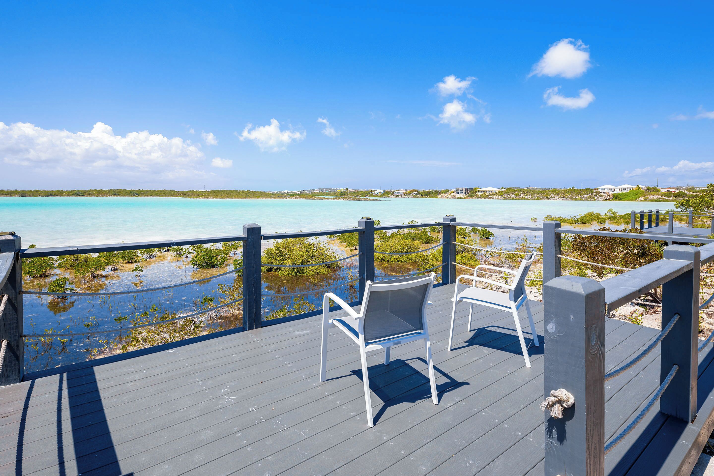 A wooden deck with two white chairs overlooking a turquoise sea and a beach.