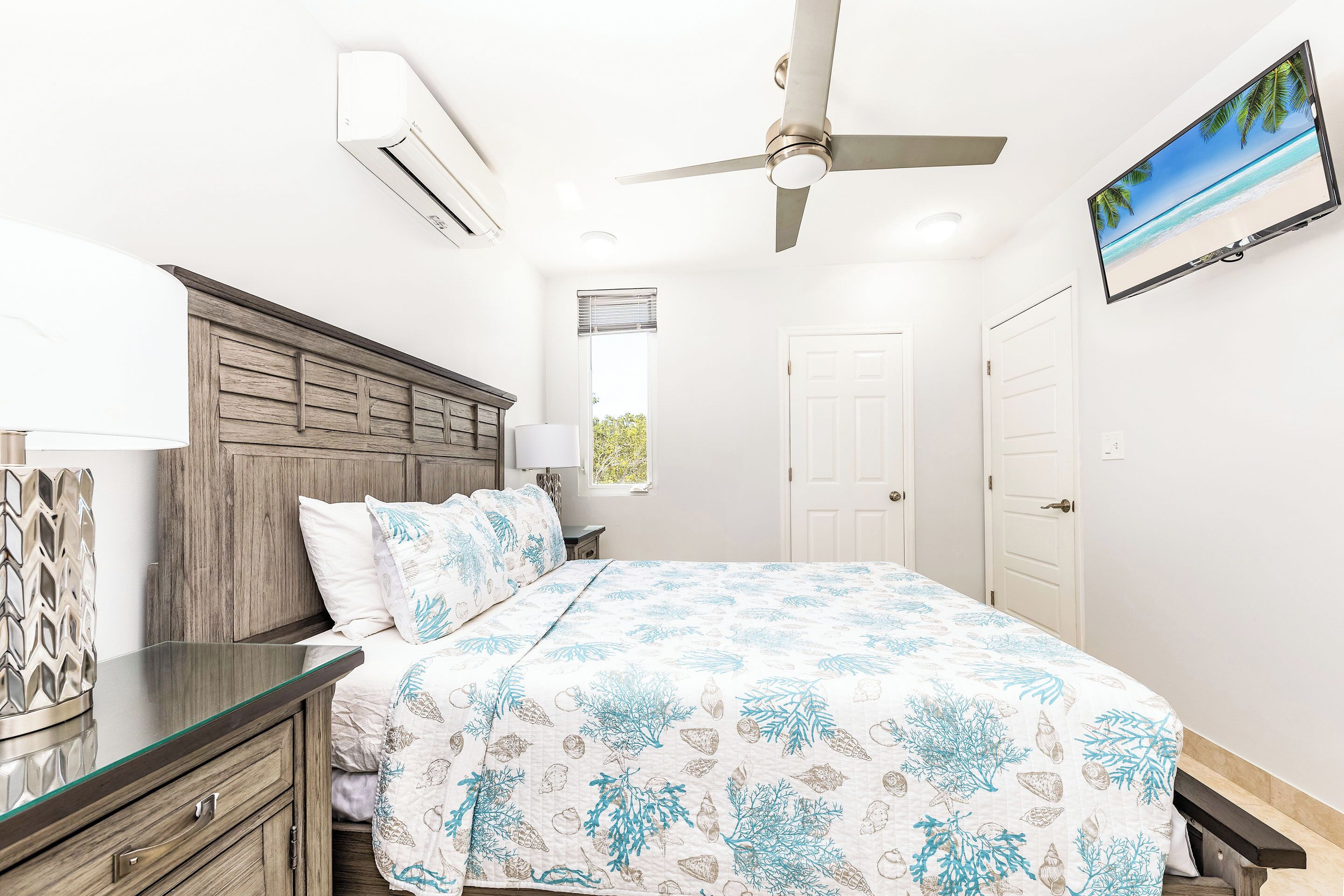 A bedroom with a bed, nightstands, a ceiling fan, an air conditioning unit, and a TV on the wall.