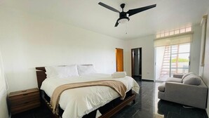 Ein Schlafzimmer mit einem Bett, einem Deckenventilator, einem Nachttisch, einem Sofa und einer Tür zu einem anderen Raum.