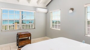 A bedroom with a large bed, two windows with blinds, an air conditioning unit, and a small wooden nightstand. - Bright & Roomie Bottle Creek Apts (Bottle Creek)