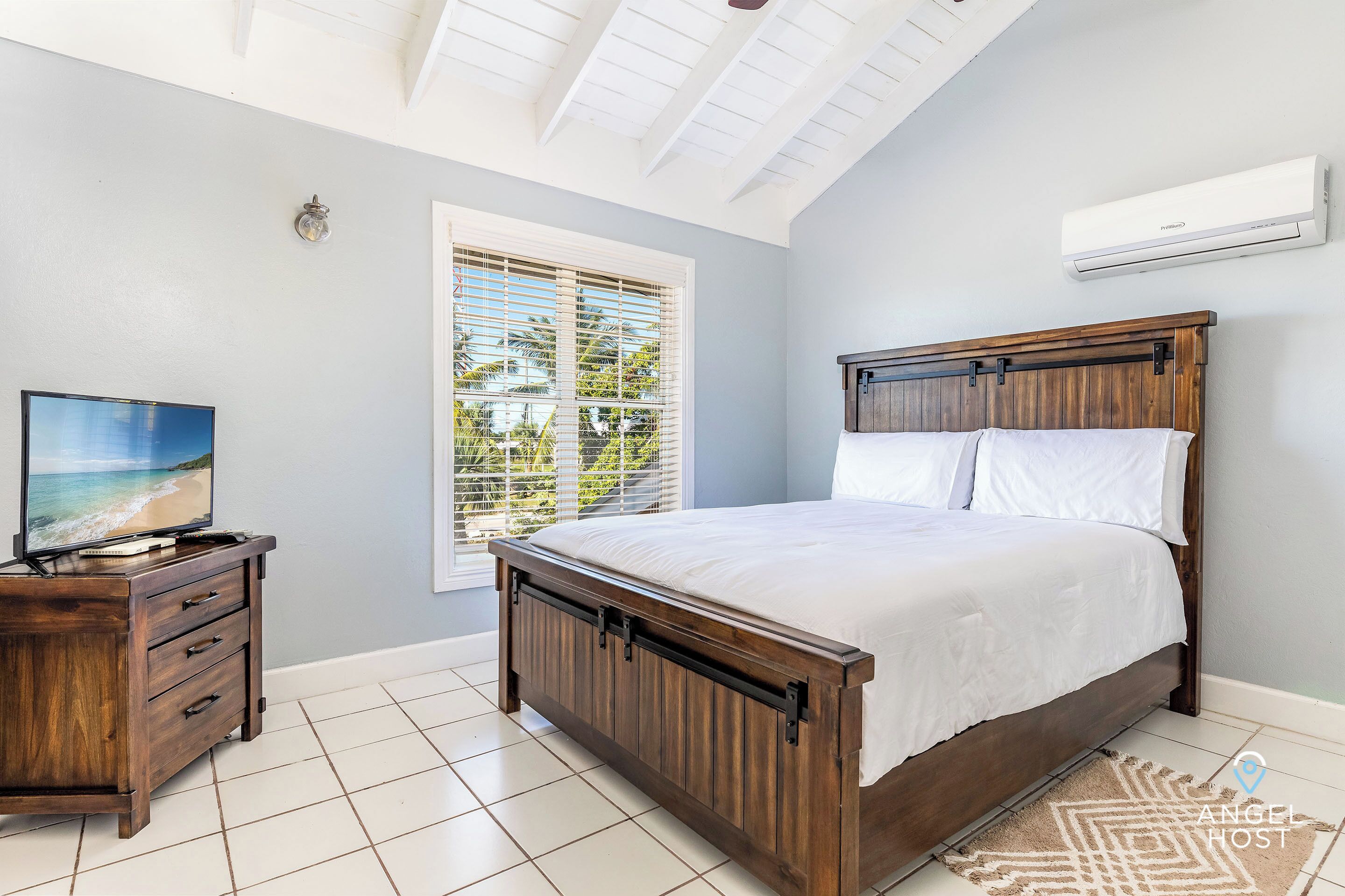 Et soveværelse med en træseng, et fjernsyn på en trækommode og et vindue med persienner.