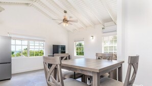 A spacious dining area with a wooden table and chairs, large windows with blinds, and a ceiling fan. - Bright & Roomie Bottle Creek Apts (Bottle Creek)