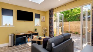 Una sala de estar con sofá, televisión, estantería y puerta corrediza de vidrio a un jardín.