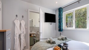 Un dormitorio con cama, televisor, ventana con cortinas, baño y armario.