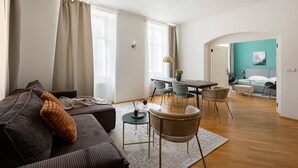 Een ruime woonkamer met een bank, stoelen, een eettafel en een keuken op de achtergrond.