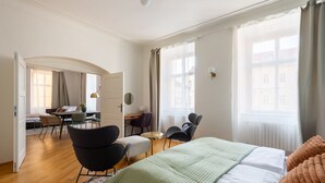 Een hotelkamer met een bed, een bureau, twee stoelen, een klein tafeltje en een raam met gordijnen.