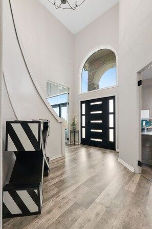 Un passadís ample amb una escala moderna, una porta amb marc negre i una vista del cel a través d'una finestra apuntada.