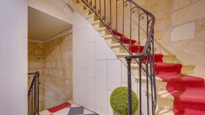 A staircase with red carpeted steps and a metal railing, leading to a room with a checkered floor and a potted plant.