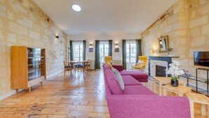 A spacious living room with a wooden floor, a large sofa, a dining table with chairs, and a fireplace.