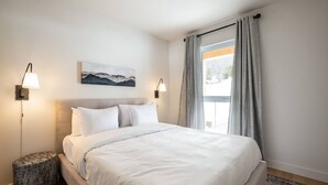Habitación de hotel con una cama grande, dos lámparas de noche, un cuadro en la pared y una ventana con cortinas.