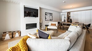 Una sala de estar moderna con un sofá, sillones, una chimenea, un comedor y un televisor montado en la pared.