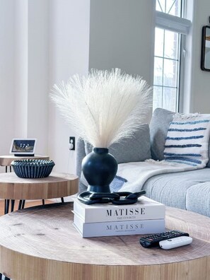 A modern living room with a round wooden coffee table, a vase with white feathers, a stack of books titled 'MATISSE', and a remote control. - Mississauga Home Away from Home (Mississauga)