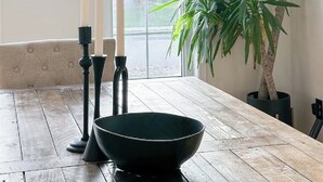 Ein Essbereich mit einem Holztisch, schwarzen Kerzenhaltern und einer großen Kübelpflanze.