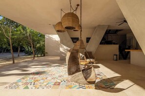 An outdoor area with a patterned floor, hanging wicker chairs, and a staircase.