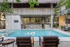 A pool area with lounge chairs, a thatched roof structure, and a patterned wall.