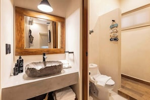 Un baño con un espejo de marco de madera, un lavabo de piedra, un inodoro y un perchero con indicaciones.